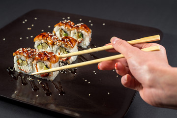 Hand with chopsticks for sushi taking a roll on dark background