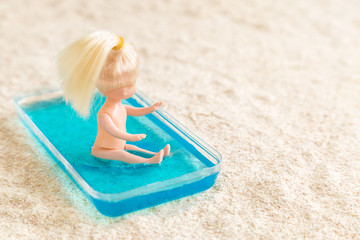 Girl sitting in small swimming pool for children at the sandy beach abstract.