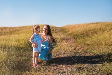 Young mother and daughter, hugging and playing in a golden field of sunshine.