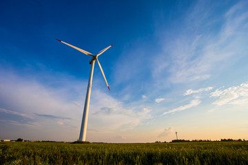 Fototapeta premium Sunny evening in countryside. Wind turbine in blue sky background. Renewable energy concept