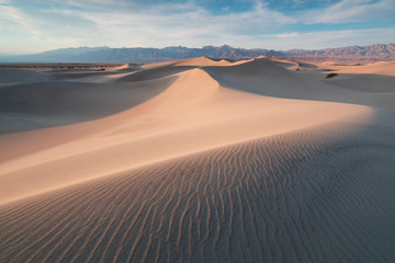 Obraz na płótnie Canvas Early Morning Sunlight Over Sand Dunes And Mountains At Mesquite flat dunes, Death Valley National Park, California USA Stovepipe Wells sand dunes, very nice structures in sand Beautiful background