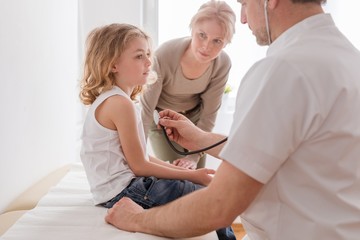 Pediatrician examining cute boy with pneumonia, worried mother behind them