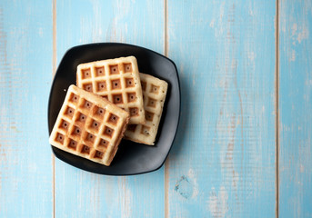 Freshly baked waffles on plate on wood background,top view