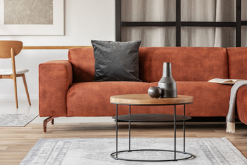 Black vase on wooden coffee table in chic living room interior with comfortable sofa