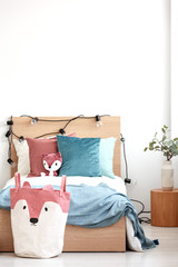 Velvet pastel pink and turquoise pillows and toy fox on single wooden bed with white bedding and blanket