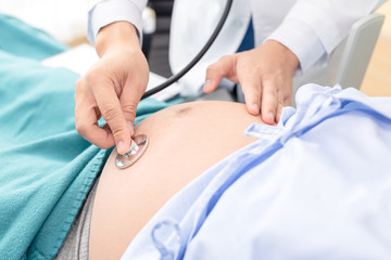 Doctor using hands and stethoscope listening to patient, pregnant tummy for health check up.