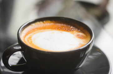 close up modern hot black coffee the cappuccino on dark background with coffee bubble foam pattern and texture in black cup looking and feel so delicious on glasses table in coffee shop.