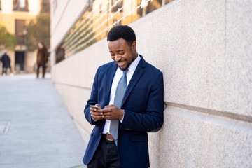 Young handsome businessman using mobile phone app sending message outside office in urban city