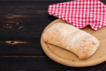 Loaf of ciabatta bread on a cutting board on the dark wooden table