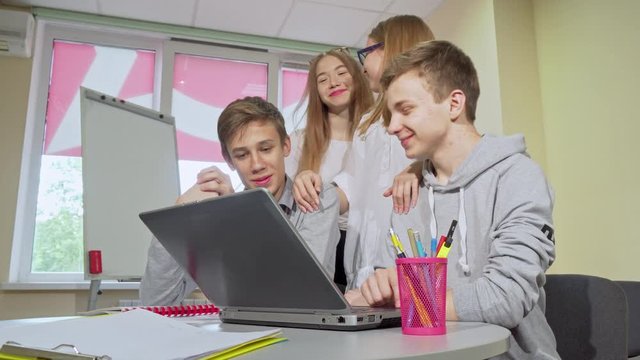 Group of teen students working on laptop together. Young cheerful teenage boys and girls studying together at high school library. Friendship, communication, e-learning concept