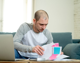 Upset man in stress paying credit card online debts and counting finance with laptop and bank papers