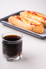 Single glass of cola drink with two hot dog fast food junk fresh sausage cheese sauce isolated on baking tray white background