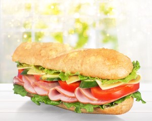 Long baguette sandwich with lettuce, vegetables, ham, and cheese on white background