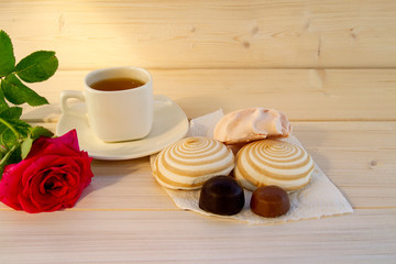Delicate multicolored marshmallows on white openwork plate. Still life with marshmallows, a Cup of tea and a rose on vintage background.