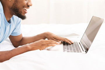 Black man blogger typing on laptop in bed