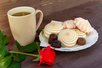 Delicate multicolored marshmallows on white openwork plate. Still life with marshmallows, a Cup of tea and a rose on vintage background.