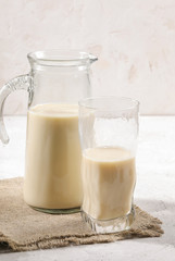 Close-up decanter and glass of oat milk on burlup napkin on white background.