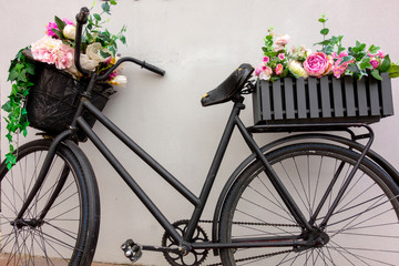 Fototapeta na wymiar Retro bicycle as a flowerbed decoration outside element. Black aged bike stays against the wall with two garden baskets with beauty flowers. Art decor closeup
