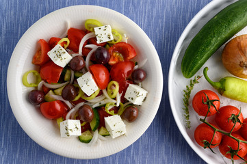 Traditional greek salad in white plate on blue matting.