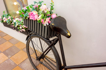 Fototapeta na wymiar Retro bicycle as a flowerbed decoration outside element. Black aged bike stays against the wall with two garden baskets with beauty flowers. Art decor closeup macro