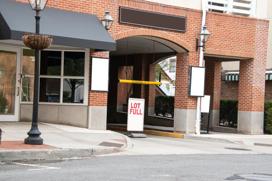 Street entrance to a parking garage in a building. There is a lot full sign blocking the entrance. There are several blank signs