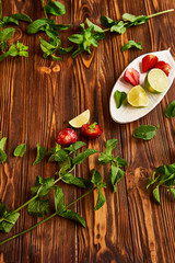 cooking of cooling summer cocktail with strawberries, ice and mint and around the berries are ripe fresh strawberries and lime