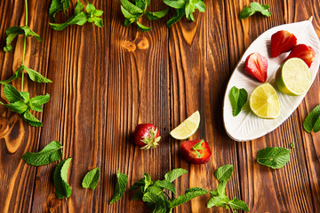 cooking of cooling summer cocktail with strawberries, ice and mint and around the berries are ripe fresh strawberries and lime