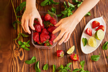 cooking of cooling summer cocktail with strawberries, ice and mint and around the berries are ripe fresh strawberries and lime