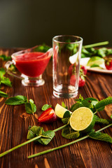 empty glass for smoothies. lime, strawberry, mint - ingredients for making lemonade on brown wooden table