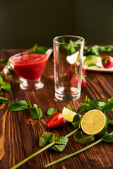 cooking of cooling summer cocktail with strawberries, ice and mint and around the berries are ripe fresh strawberries and lime