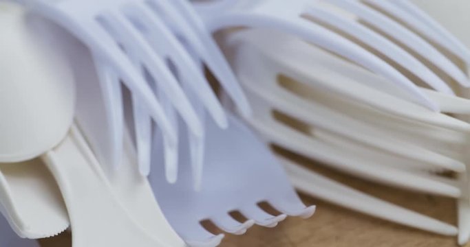 A bunch of single use plastic forks and spoons lying on a wood surface