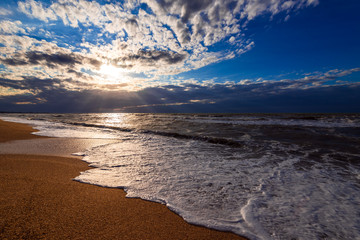 A beach with golden sand, small waves and a beautiful dramatic sky