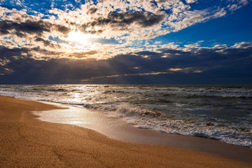 A beach with golden sand, small waves and a beautiful dramatic sky