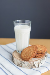 still life of round brown wholegrain flour cookies and milk glass on striped white napkin on wooden table, side view of vertical stock photo image