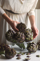Woman wearing in pastel dress put in the basket fresh artichokes. Organic produce or local market...