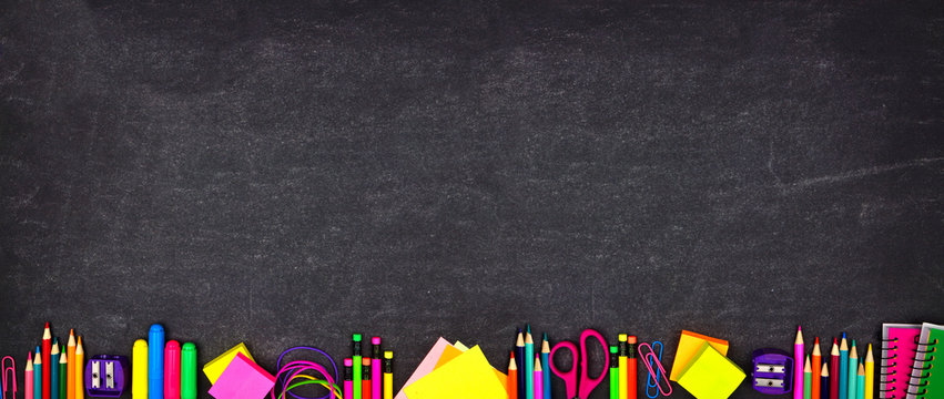School supplies bottom border banner. Top view on a chalkboard background with copy space. Back to school concept.