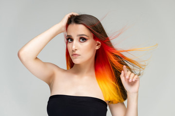 A close-up portrait photo of a fashionable hairstyle red-yellow in studio on a white background. The pretty brunette model with beautiful make-up has beautiful flowing colorful hair.