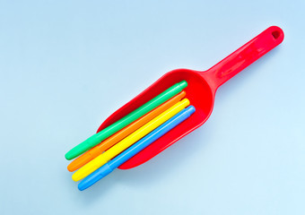 Colorful markers in red plastic toy shovel, against light blue background.