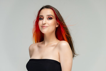 Fototapeta premium A close-up portrait photo of a fashionable hairstyle red-yellow in studio on a white background. The pretty brunette model with beautiful make-up has beautiful flowing colorful hair.