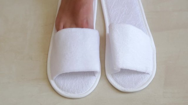 Closeup top view of pair of white new slippers in room of hotel. Woman with beautiful french white and pink pedicure putting on slippers. Real time full hd video footage.