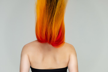 Obraz premium A close-up portrait photo of a fashionable hairstyle red-yellow in studio on a white background. The pretty brunette model with beautiful make-up has beautiful flowing colorful hair.