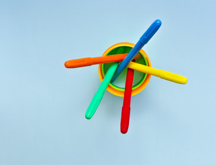 Color markers in colorful container, against light blue background.