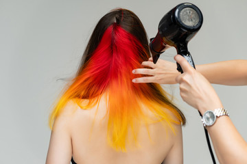 Fototapeta premium A close-up portrait photo of a fashionable hairstyle red-yellow in studio on a white background. The pretty brunette model with beautiful make-up has beautiful flowing colorful hair.