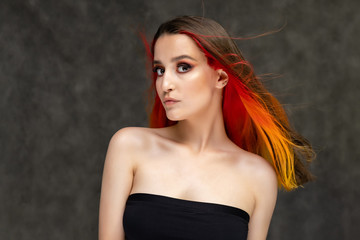 Naklejka premium A close-up portrait photo of a fashionable hairstyle red-yellow in studio on a gray background. The pretty brunette model with beautiful make-up has beautiful flowing colorful hair.
