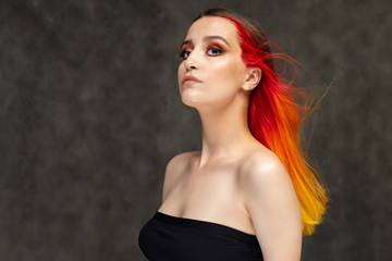 Naklejka premium A close-up portrait photo of a fashionable hairstyle red-yellow in studio on a gray background. The pretty brunette model with beautiful make-up has beautiful flowing colorful hair.