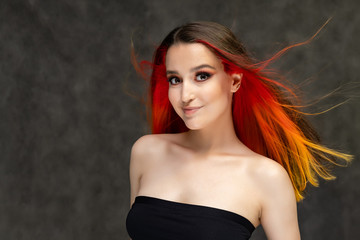 Fototapeta premium A close-up portrait photo of a fashionable hairstyle red-yellow in studio on a gray background. The pretty brunette model with beautiful make-up has beautiful flowing colorful hair.