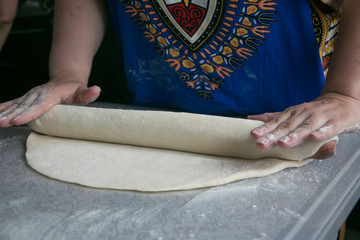 Women's hands rolling a rolling pin on a glass table dough