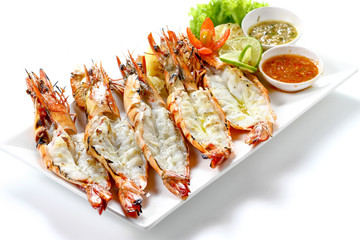 Grilled 5 black tiger shrimps with boiled potatoes, slice of lime, tomato fresh vegetables and 2 chili seafood sauce on white square plate isolated on white background with shadow high angle side view
