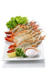 Grilled 5 black tiger shrimps with boiled potatoes, slice of lime, tomato fresh vegetables and chili seafood sauce on white square plate isolated on white background Portrait high angle top view