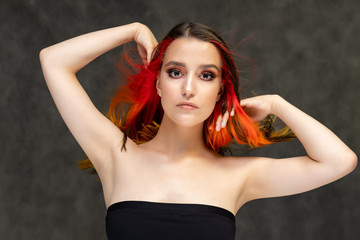 Fototapeta premium A close-up portrait photo of a fashionable hairstyle red-yellow in studio on a gray background. The pretty brunette model with beautiful make-up has beautiful flowing colorful hair.
